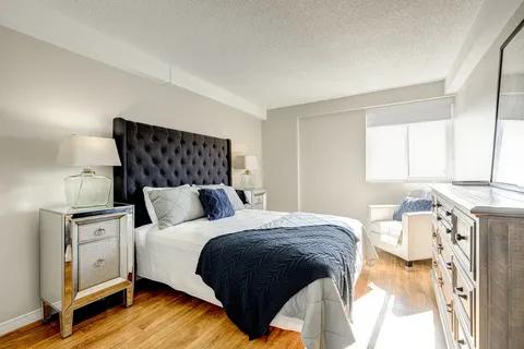 Bedroom with a padded headboard, blue bedding, dresser and white armchair
