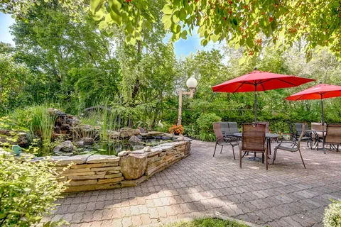 Paved garden patio with tables, chairs, red umbrellas and a raised pond