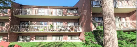 Brick residence with balconies beside a lawn, shrubs and a large tree