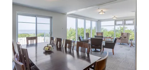 Room with a large wooden table, chairs and seating beside wraparound windows