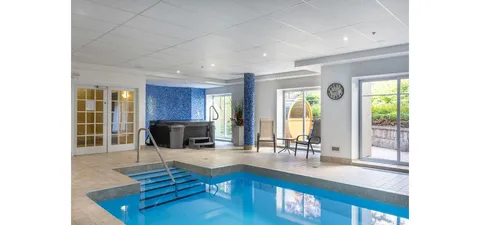 Indoor swimming pool with handrails, a hot tub and large windows