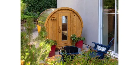 Wooden barrel sauna beside a garden and blue outdoor chair