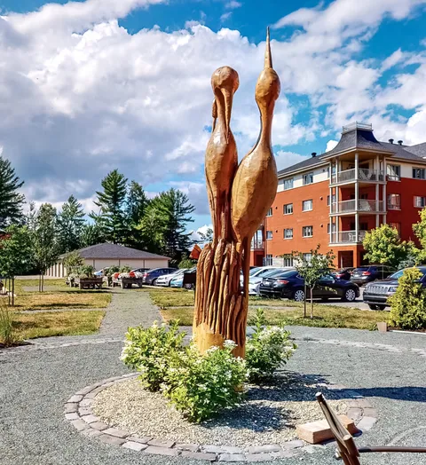 Wooden bird sculptures beside a flower bed and path in front of a residence