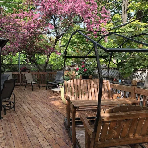 Wooden garden swing on a deck beneath flowering branches.