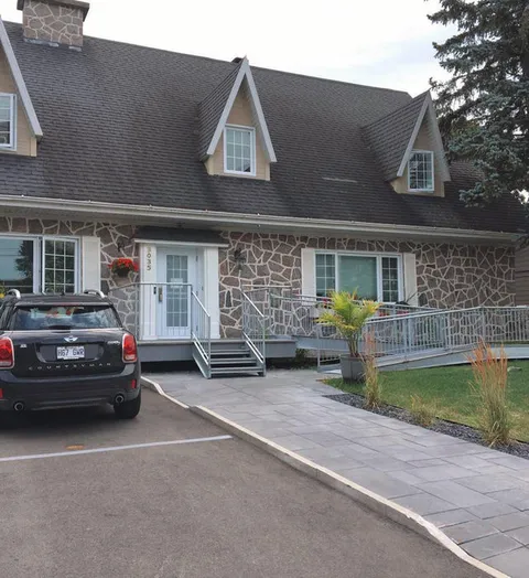 Stone-front residence with dormers, an entrance ramp and driveway.