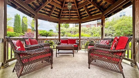 Inside a wooden gazebo with woven armchairs and red cushions
