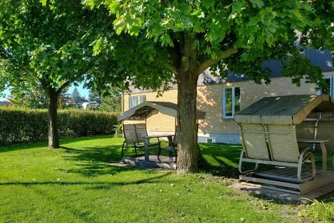 Lawn with two covered garden swings beneath trees beside the building.