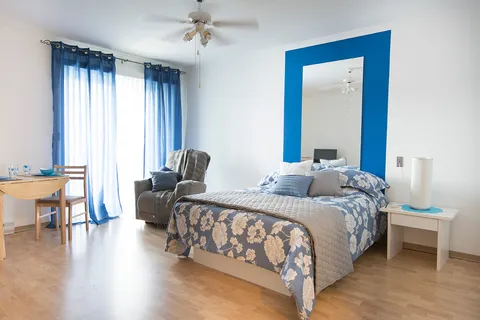 Bedroom with blue floral bedding, an armchair, a table and blue curtains