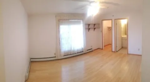 Empty room with wood flooring, a window and an adjoining doorway.