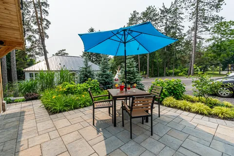 Patio with a table, wooden chairs and a blue umbrella beside planted beds