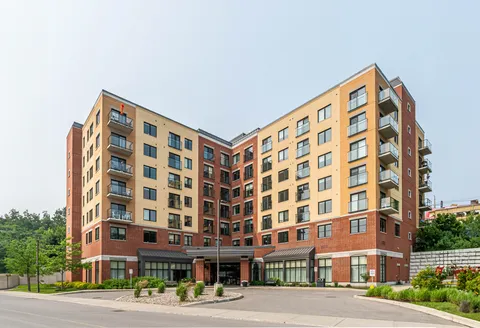 Brick and beige building with balconies, a covered entrance and planted beds