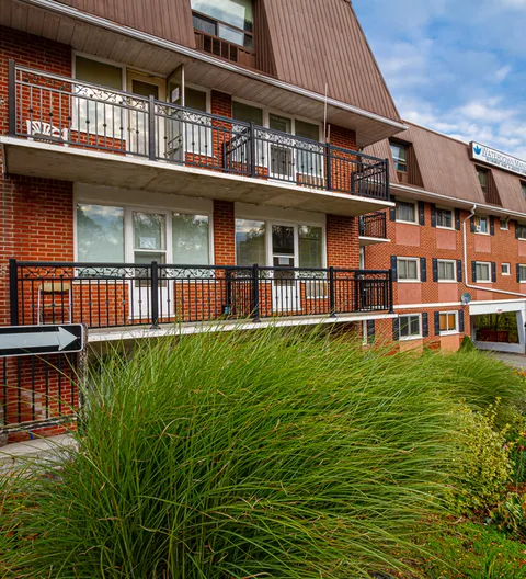 Brick residence with balconies, a sloping brown roof and ornamental grasses