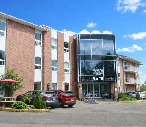 Residence exterior with a glass entrance tower, balconies and parked cars.