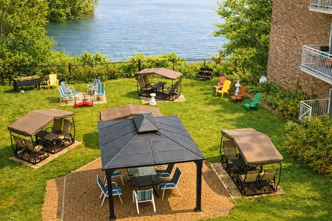 Riverside garden with a gazebo, covered swings and colourful chairs.
