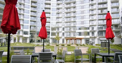Residence balconies above courtyard tables, red umbrellas and planted borders