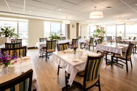 Dining room with set tables, striped chairs, flowers and large windows
