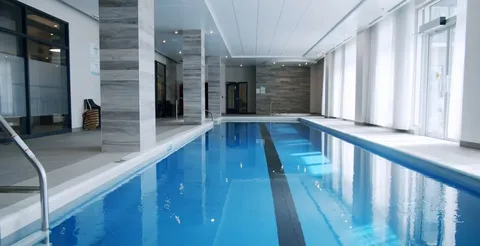 Indoor swimming pool with steps, handrails and chairs beside windows