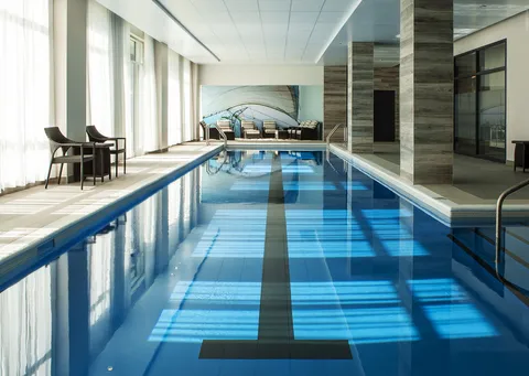 Indoor swimming pool with handrails, chairs and tall windows