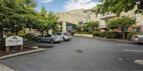Residence entrance with a driveway, parked cars, shrubs and balconies