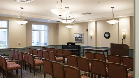 Chapel with rows of chairs, a piano and ceiling lights.