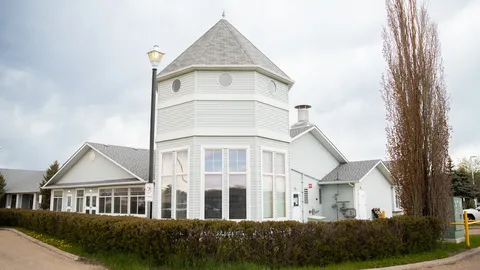 Corner tower and windows at Aspen House, beside trees and a hedge.