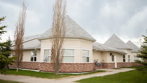 Single-storey wing with a peaked roof, brick base and lawn.