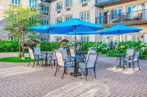 Patio tables beneath blue umbrellas beside garden beds