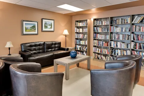 Library seating with leather chairs, a sofa, bookshelves and landscape paintings