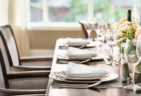 Dining table set with plates, cutlery, glassware and flowers.
