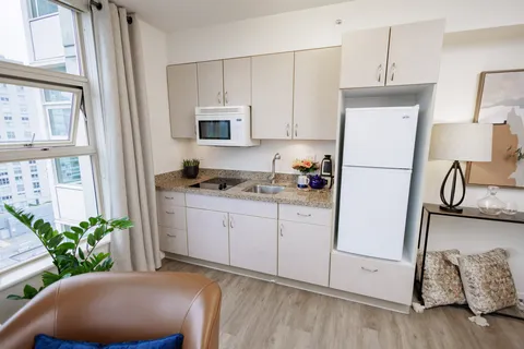 Kitchenette with white cabinets, a microwave and a fridge beside a window