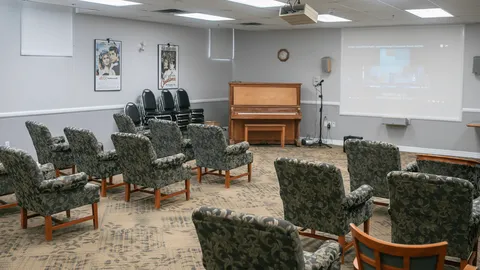 Room with rows of chairs, a piano and a wall projection screen.