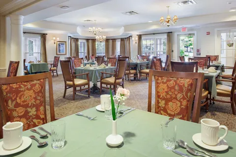 Dining room with set tables, chandeliers and patterned wooden chairs.