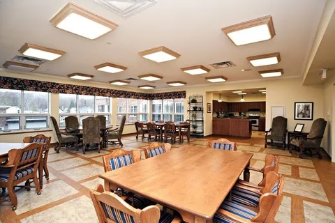 Room with wooden tables, upholstered chairs, a kitchenette and large windows