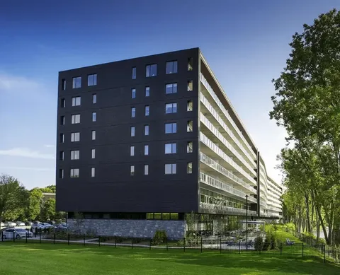 Multi-storey building with dark cladding and balconies beside a lawn