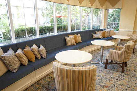 Window seating area with a long blue bench, round tables and striped armchairs