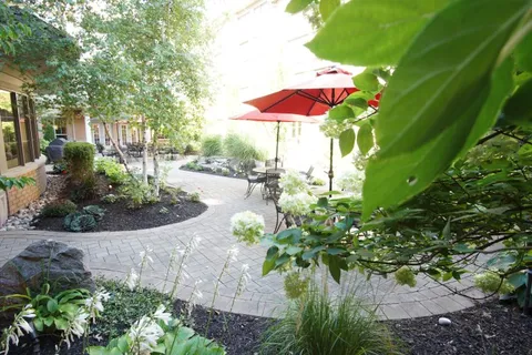 Curving paved courtyard path with planting beds, tables and red umbrellas