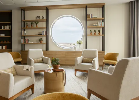 Lounge with armchairs, shelving and a round window.