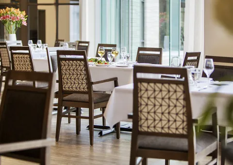 Dining room with set tables and windows overlooking the surroundings.