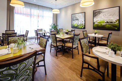 Care-unit dining room with round tables, chairs and framed pictures.
