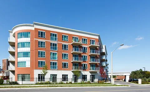 Red-brick residence with balconies and a curved corner beside a road