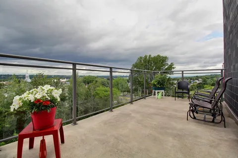 Balcony with rocking chairs, flower pots and glass railings overlooking trees