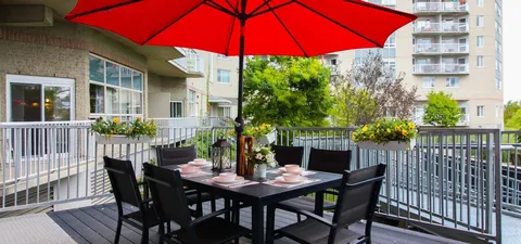 Patio table and chairs beneath a red umbrella beside flower boxes