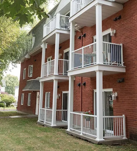 Brick building with white balconies and trees beside a lawn