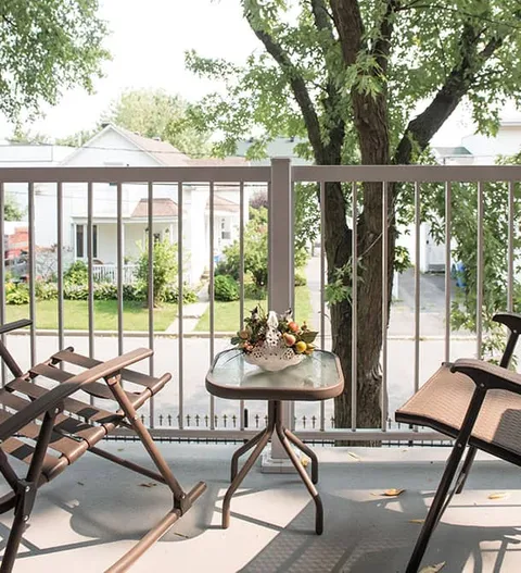 Balcony with two rocking chairs and a small table overlooking trees and neighbouring buildings