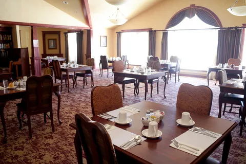Dining tables set with cups and cutlery beside tall curtained windows