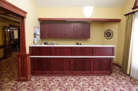 Reception counter with red wood cabinets, a wall clock and a pendant light