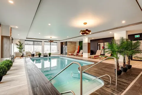 Indoor swimming pool with steps, deck chairs and potted palms