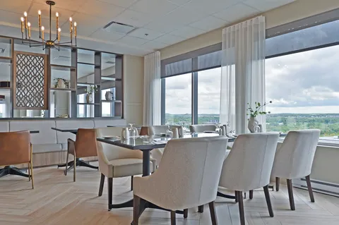 Set table with pale chairs beside a tall window and decorative shelves