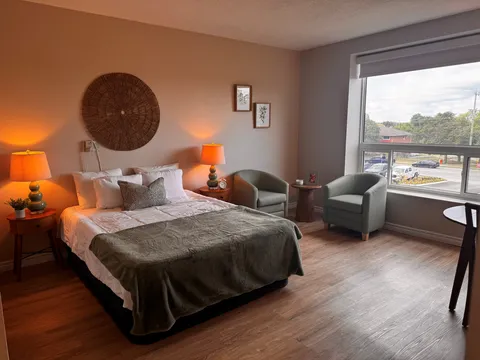 Bedroom with a bed, green armchairs, bedside lamps and a large window
