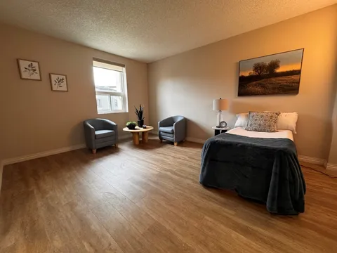 Bedroom with a single bed, two armchairs, a round table and landscape artwork